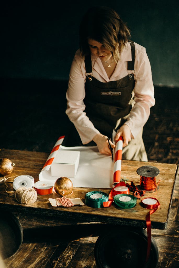 Adult woman elegantly wrapping a Christmas gift with ribbons and paper in a cozy indoor setting.