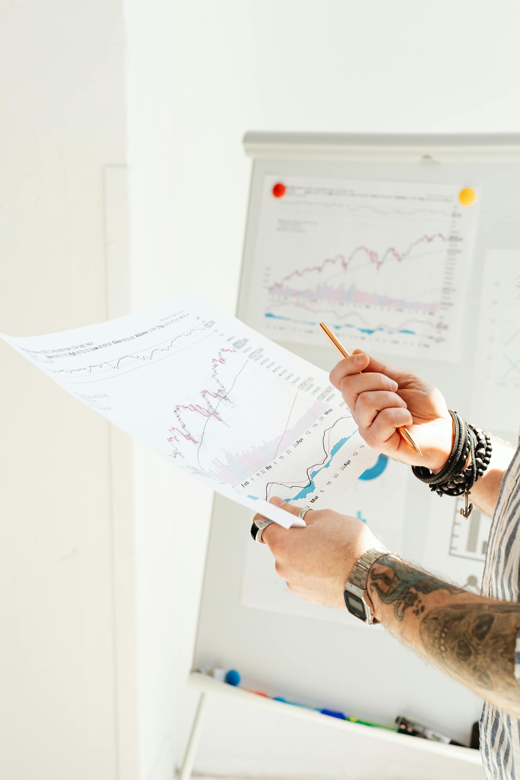 Close-up of hands holding and analyzing financial charts with a pencil in an office.