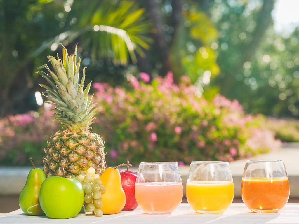 Colorful assortment of fresh fruit juices and fruits on a sunny outdoor table, perfect for summer refreshment.